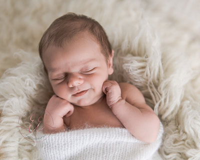 Newborn baby smiling for his first photos. Newborn photography in St Neots, Huntingdon, Cambridgeshire